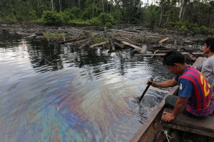 Un indígena cucama remueve el río Cuninico y observa el sedimento contaminante . Fotografía de Barbara Fraser.